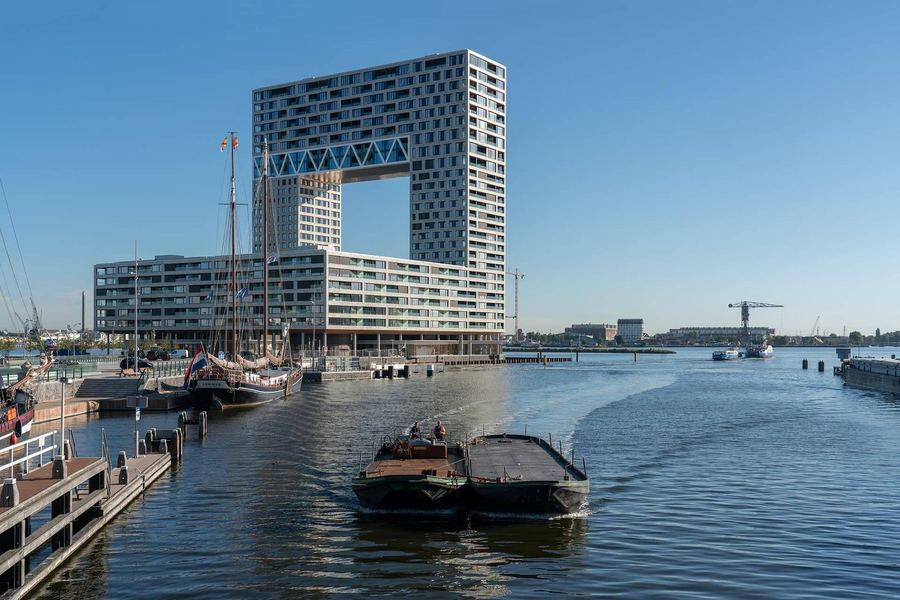 A boat crossing the IJ in Amsterdam on a bright day, the Pontsteiger building on the waterfront