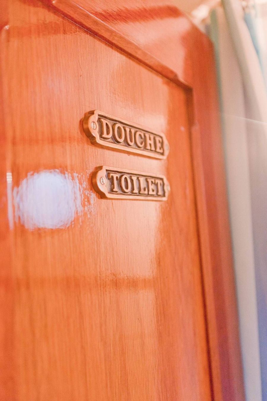Brass 'douche' and 'toilet' signs on a varnished wooden door