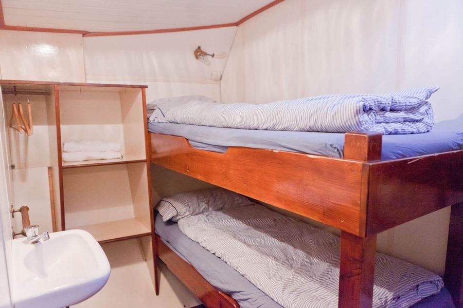 Two-person cabin with a wooden double bunk and a wash basin
