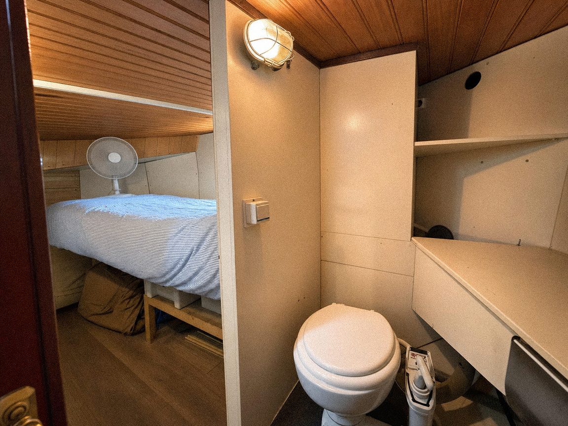 A private cabin with a made-up bed under a sloping wooden ceiling, and its own toilet