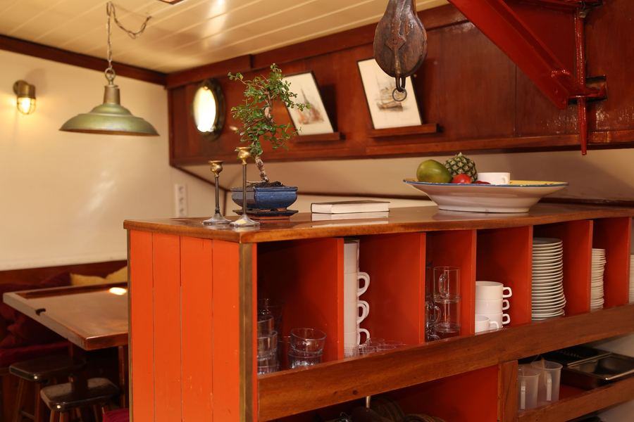 The galley bar with orange-painted shelves of glasses and cups, a brass lamp, a bonsai and a fruit bowl