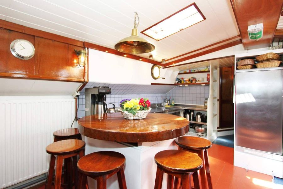 A round wooden bar table with stools beside the galley, a clock and brass lamp above