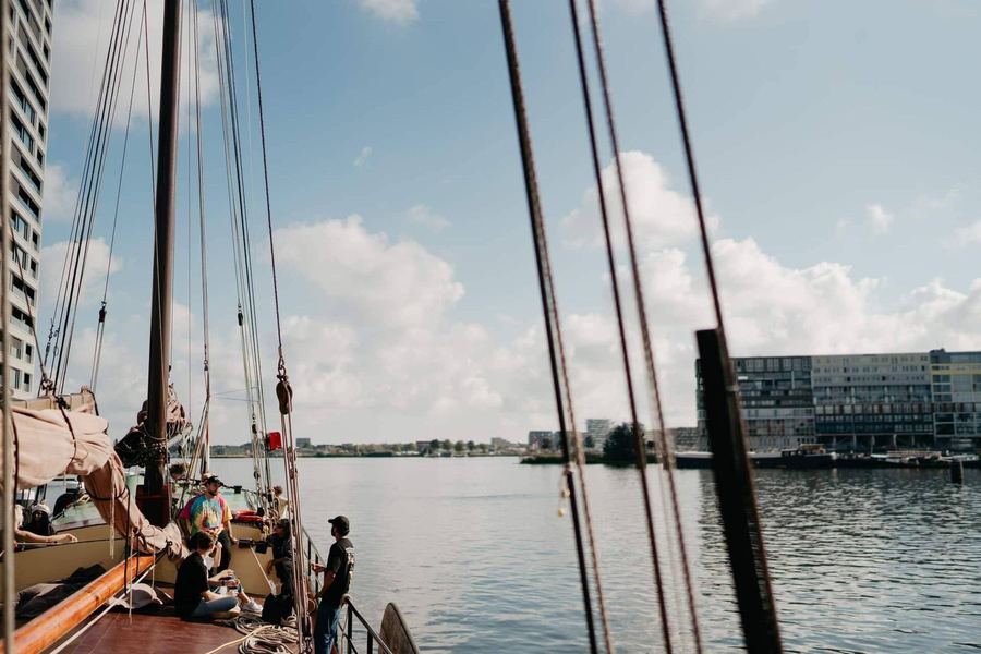 Guests relaxing on deck under the rigging with the Amsterdam waterfront in the evening light
