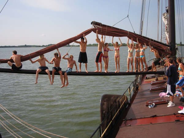 A row of guests sitting and standing on the boom, swung out over the water