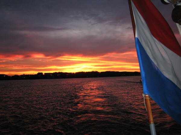 A fiery sunset over the water, the Dutch flag at the stern in the foreground